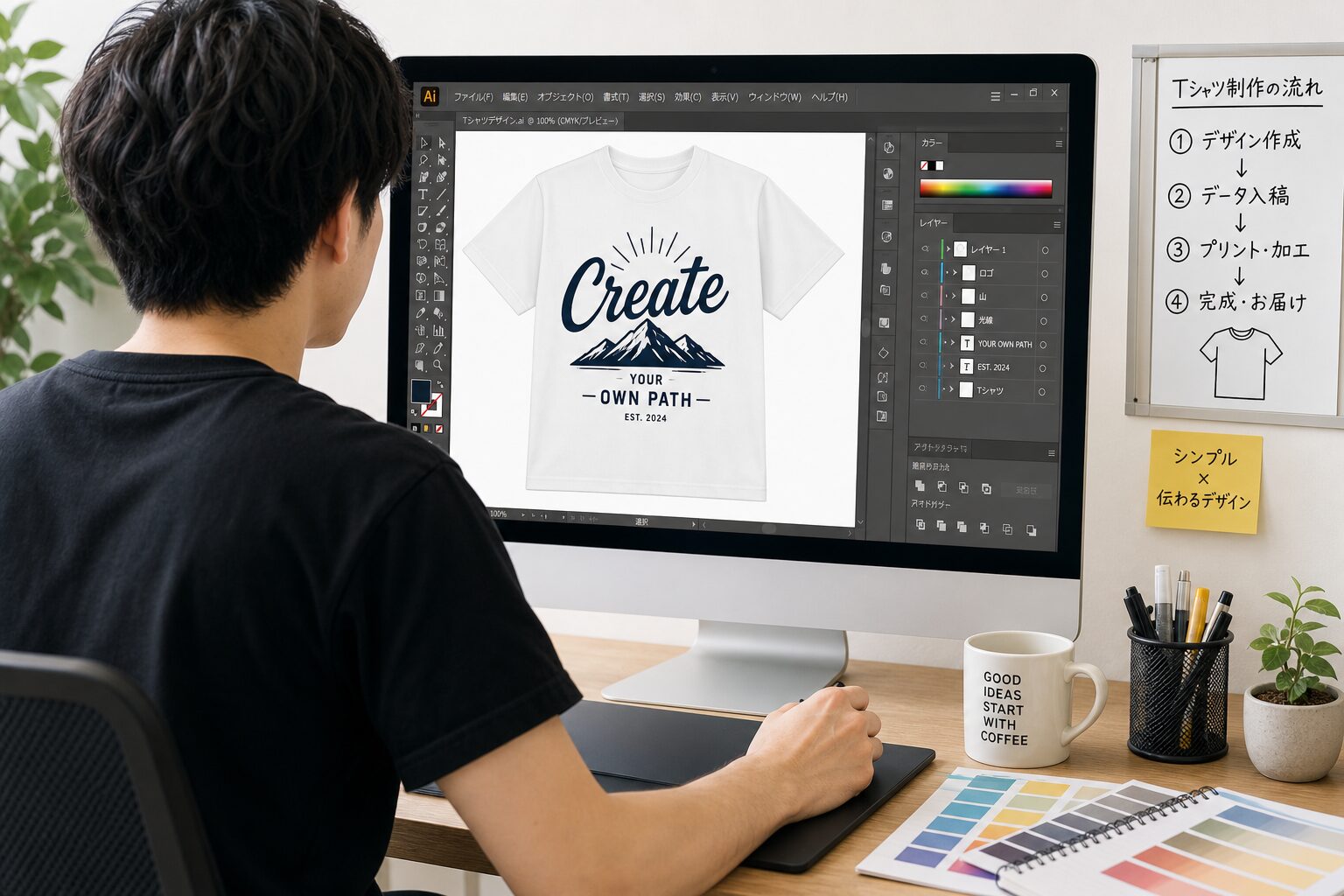 パソコンでAdobe Illustratorを操作しTシャツ用のデザインデータを作成している若いデザイナーの後ろ姿