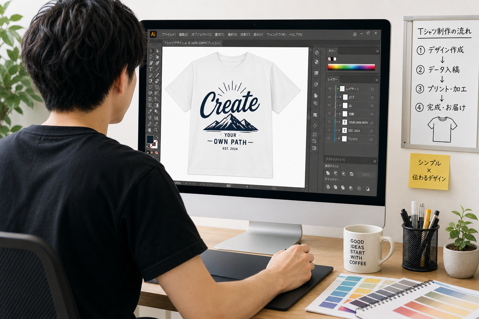 パソコンでAdobe Illustratorを操作しTシャツ用のデザインデータを作成している若いデザイナーの後ろ姿